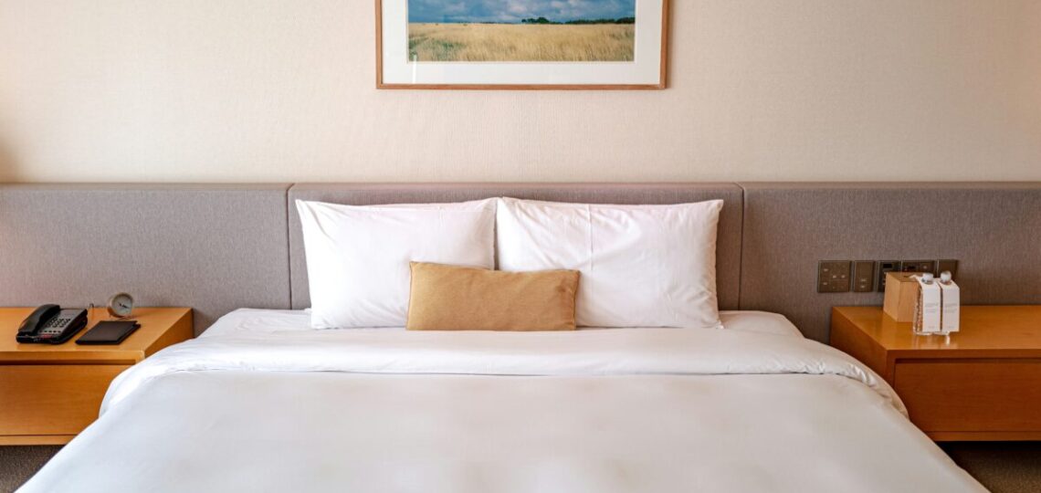 Cama de hotel con sábanas blancas de 400 hilos y cojines decorativos.